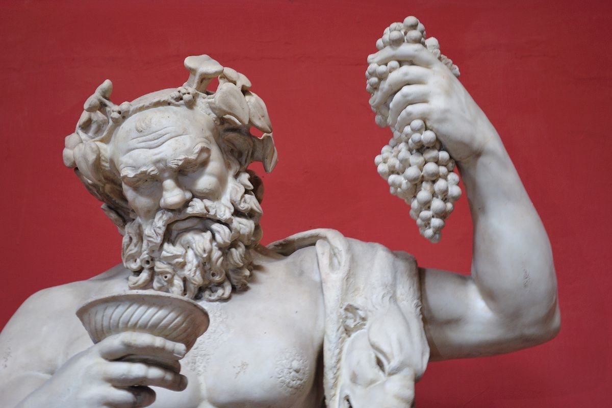 Statue of Dionysus holding grapes and a wine cup against a red background.